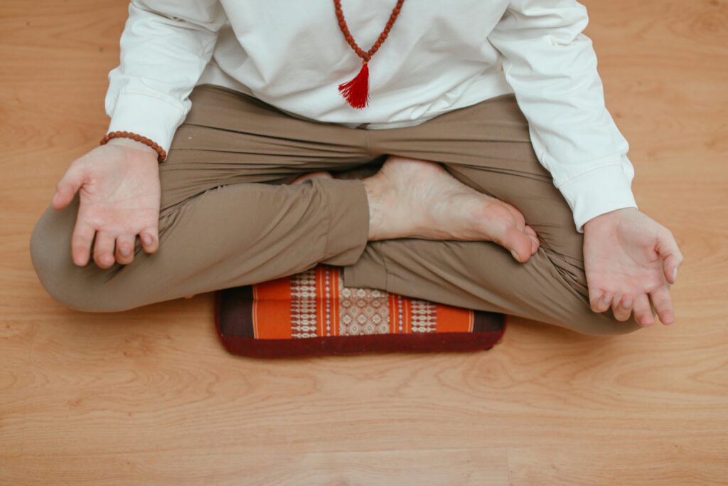 Overhead view of a man meditating at home, sitting in a yoga pose on a wooden floor.